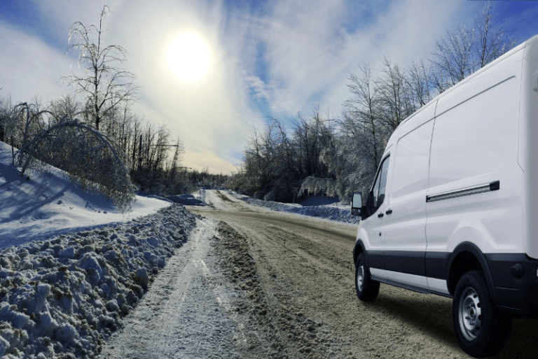 A white commercial van drives along a snowy UK road